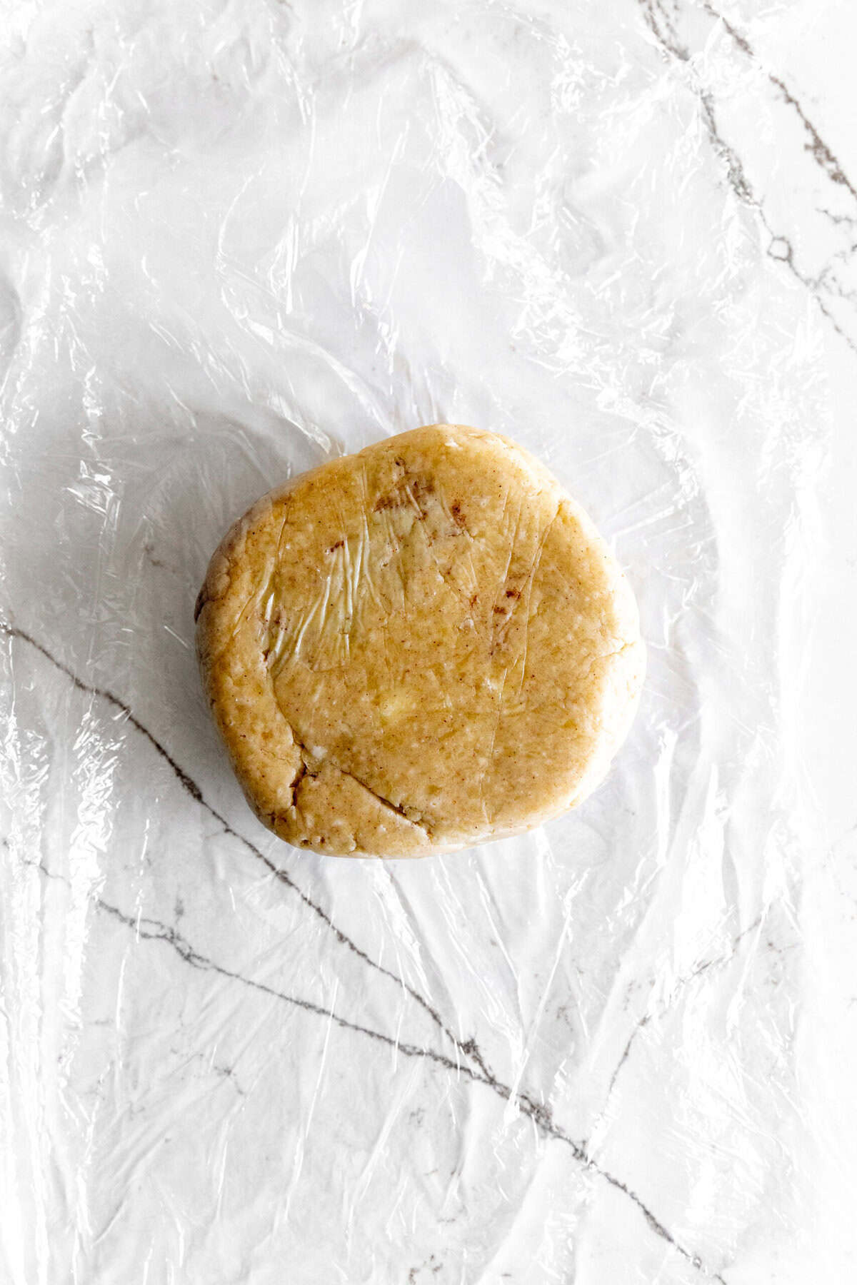 Pie crust dough wrapped in plastic on a white surface.