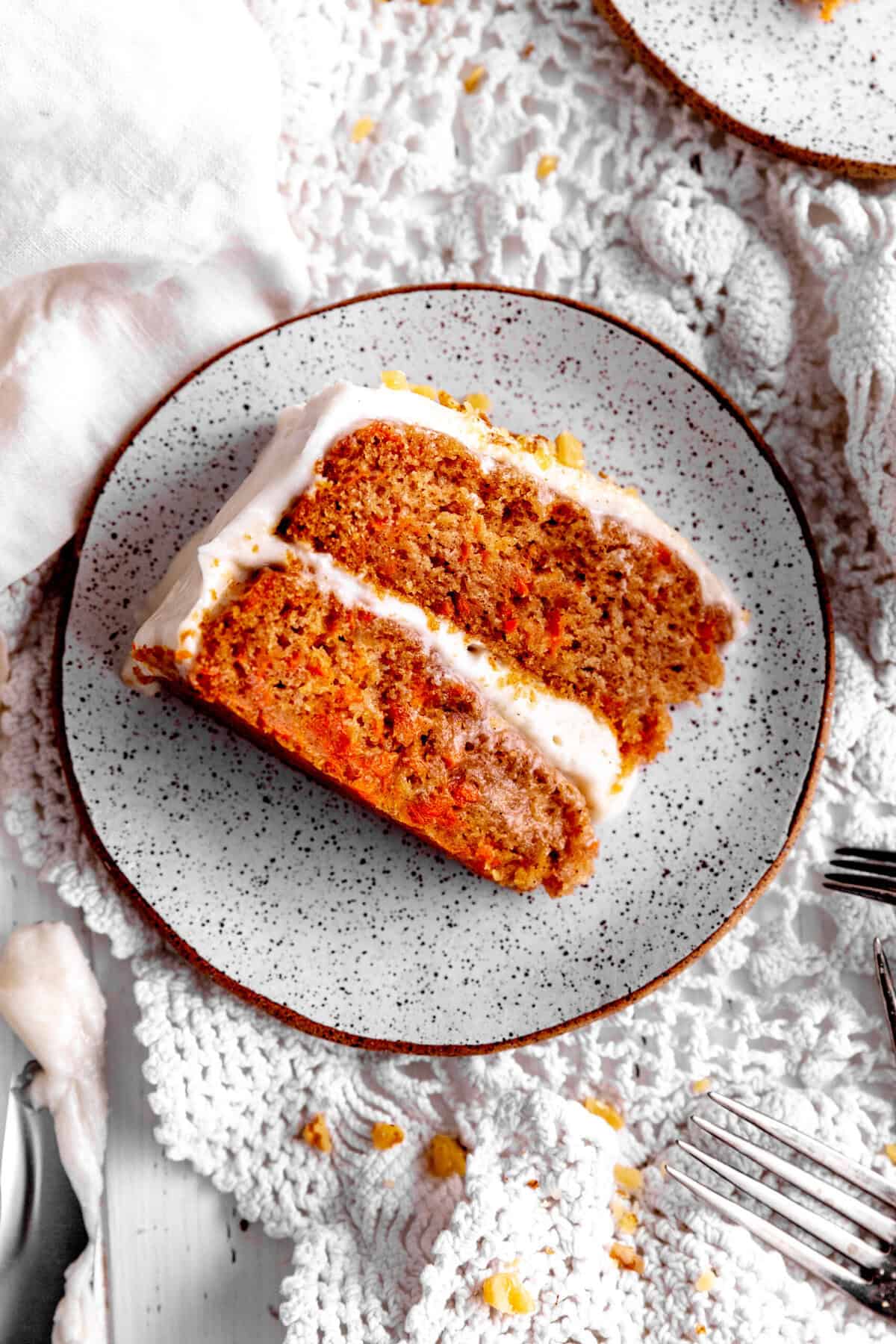 Slice of carrot cake on a white plate and several forks.