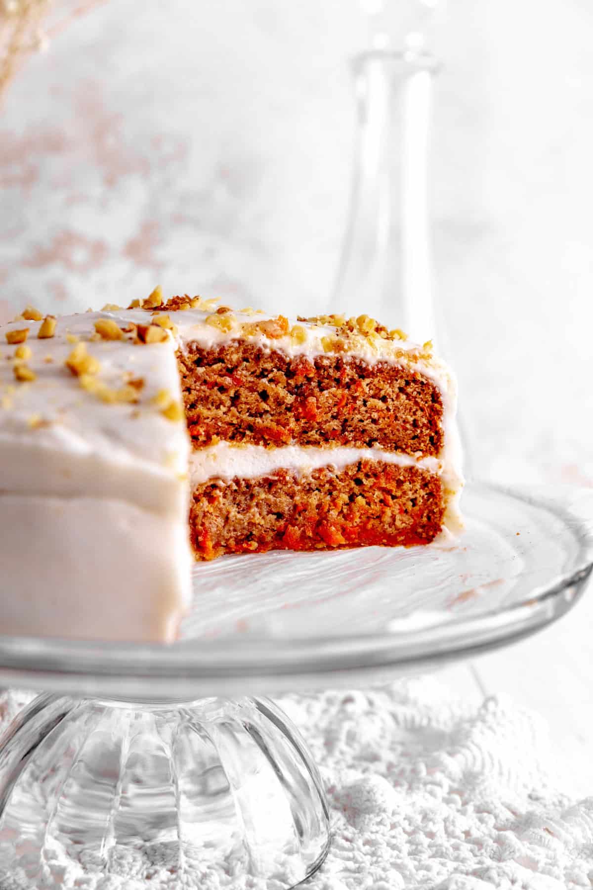 Carrot cake with slices missing on a glass cake stand.