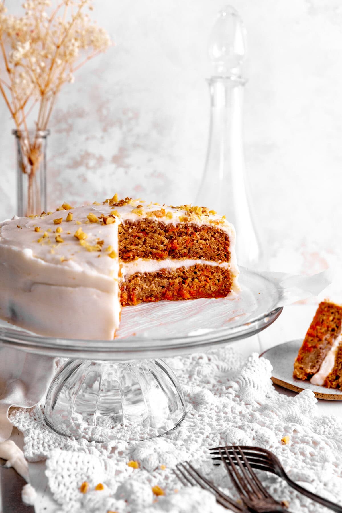 Carrot cake on a glass cake stand and slices of cake on plates.