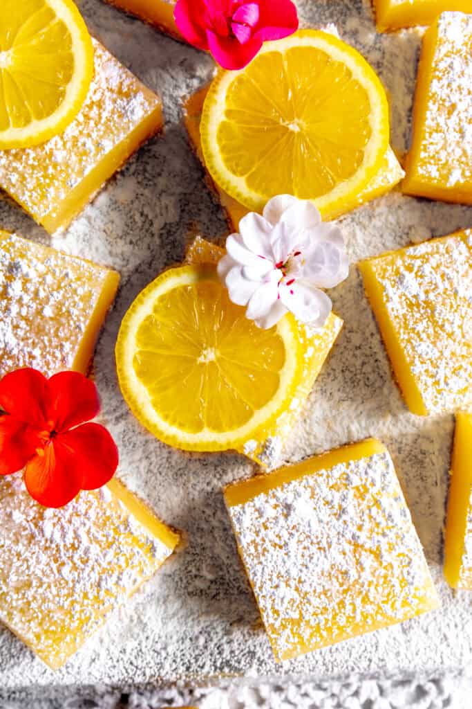 Lemon bars topped with powdered sugar, lemon slices and flower petals.