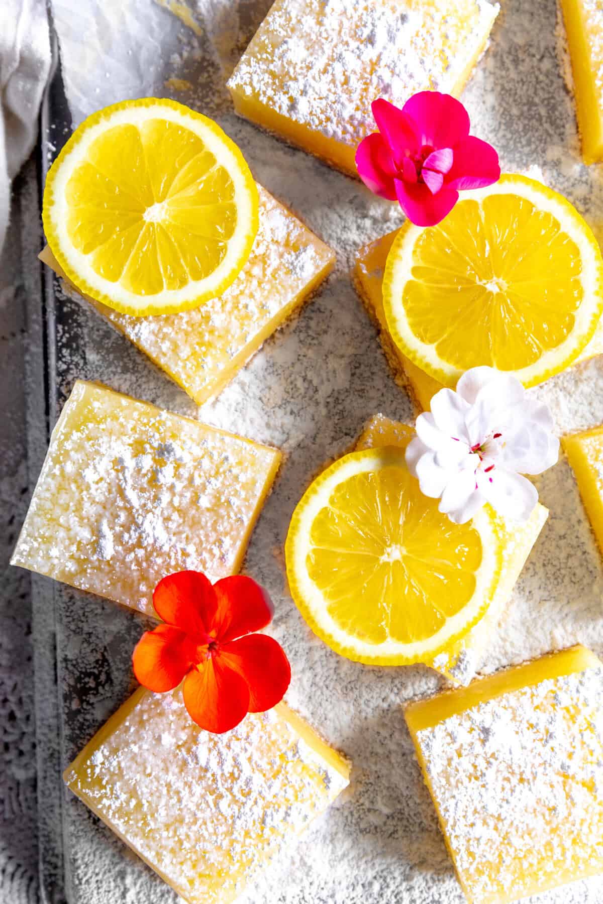 Lemon bars topped with powdered sugar, lemon slices and flower petals.
