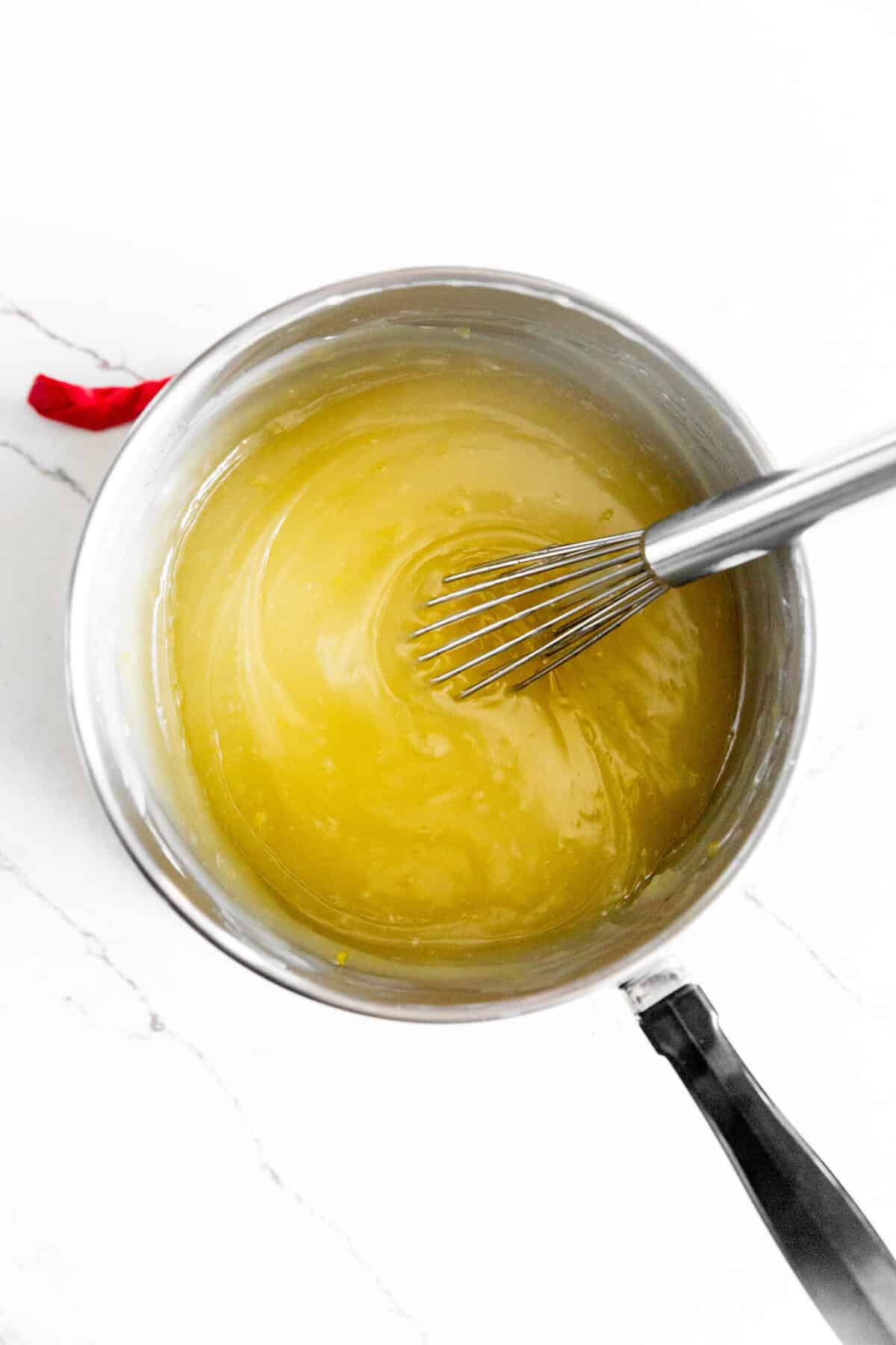 Saucepan filled with lemon bar filling and a small wire whisk.