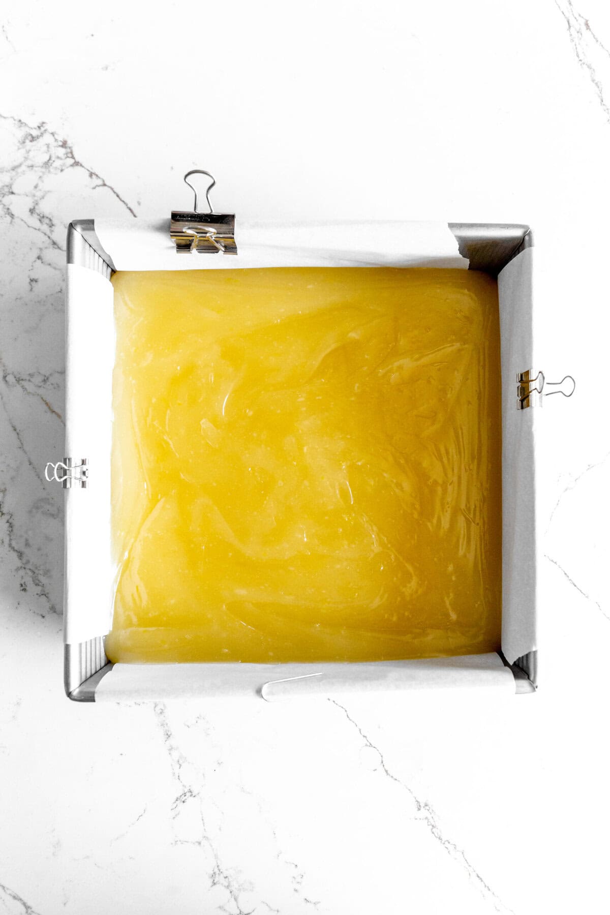 Unset lemon bars in a square pan lined with parchment paper.