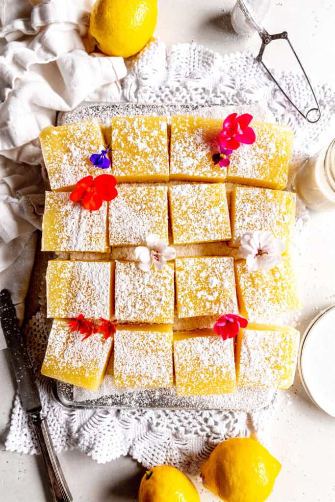 Lemon bars topped with powdered sugar, a glass of milk and lemons.