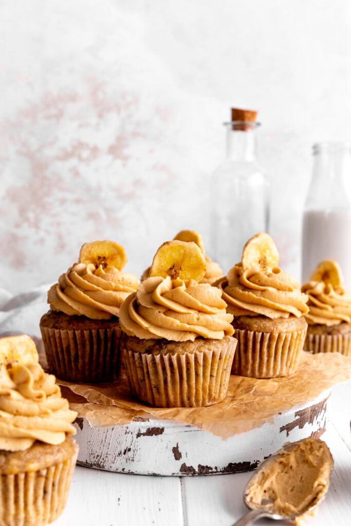 Peanut butter banana cupcakes arranged on a wooden board and a jug of milk.