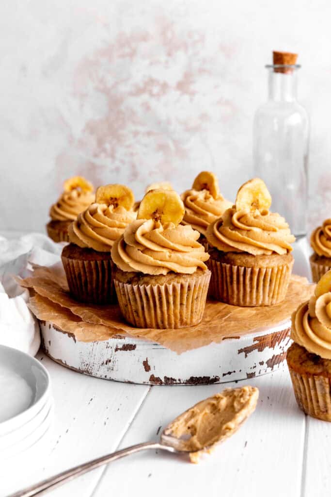 Peanut butter banana cupcakes arranged on a wooden board and a spoon covered in frosting.