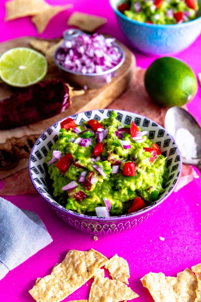 Bowl of guacamole and a wooden cutting board with guacamole ingredients.