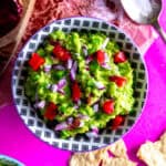 Bowl of guacamole, spoonful of salt and scattered tortilla chips.