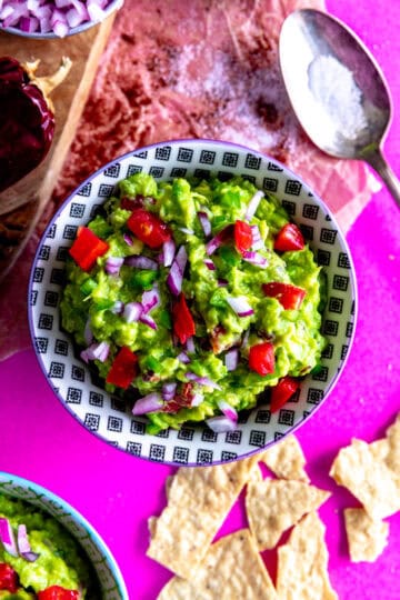Bowl of guacamole, spoonful of salt and scattered tortilla chips.