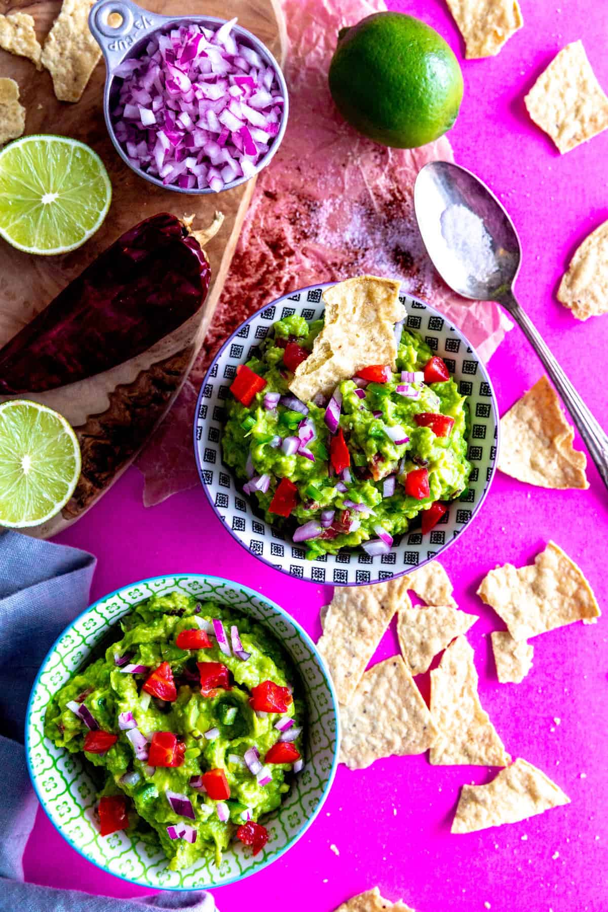 Chip dipping into a bowl of guacamole on a pink surface.