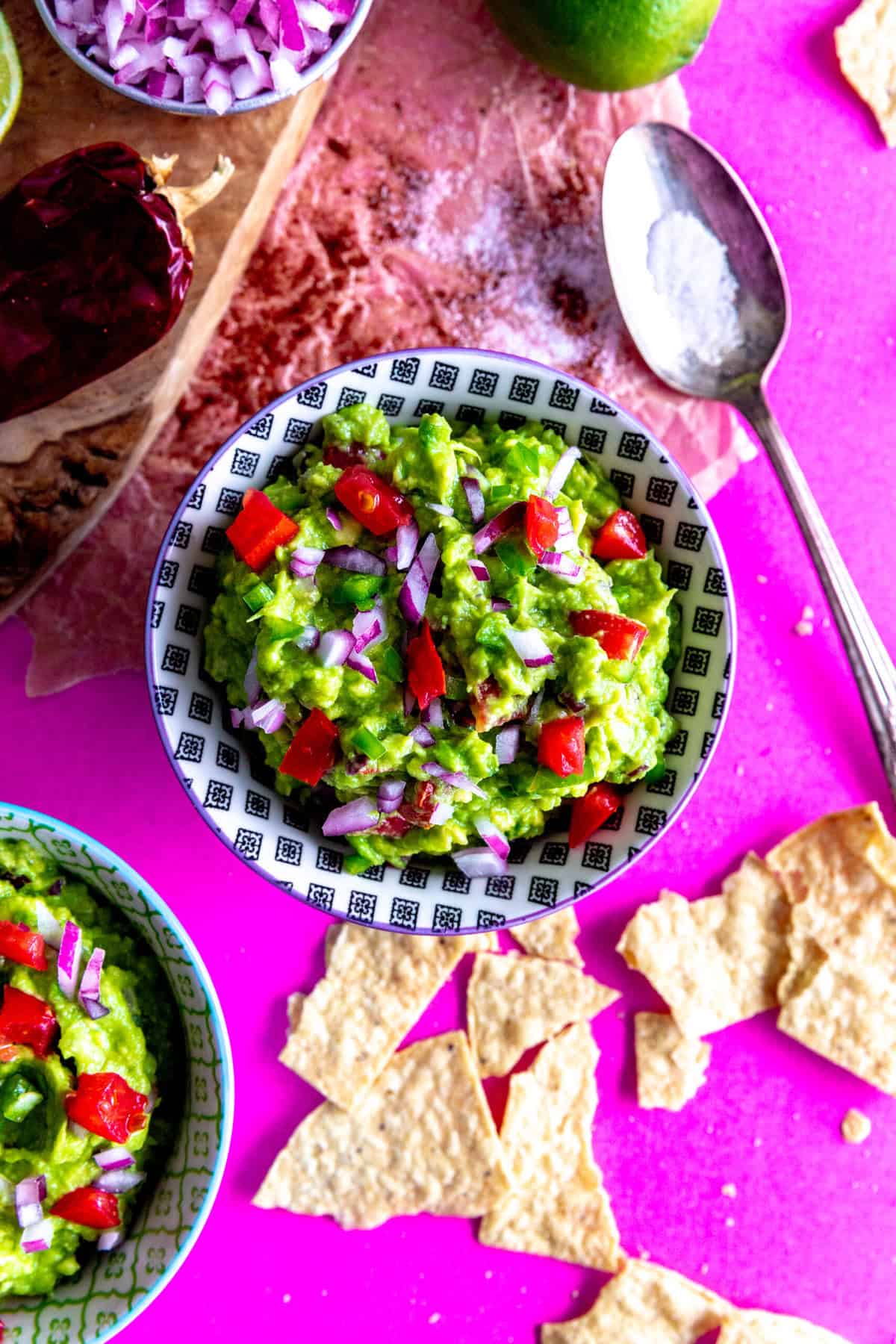 Bowl of guacamole on a pink surface with tortilla chips.