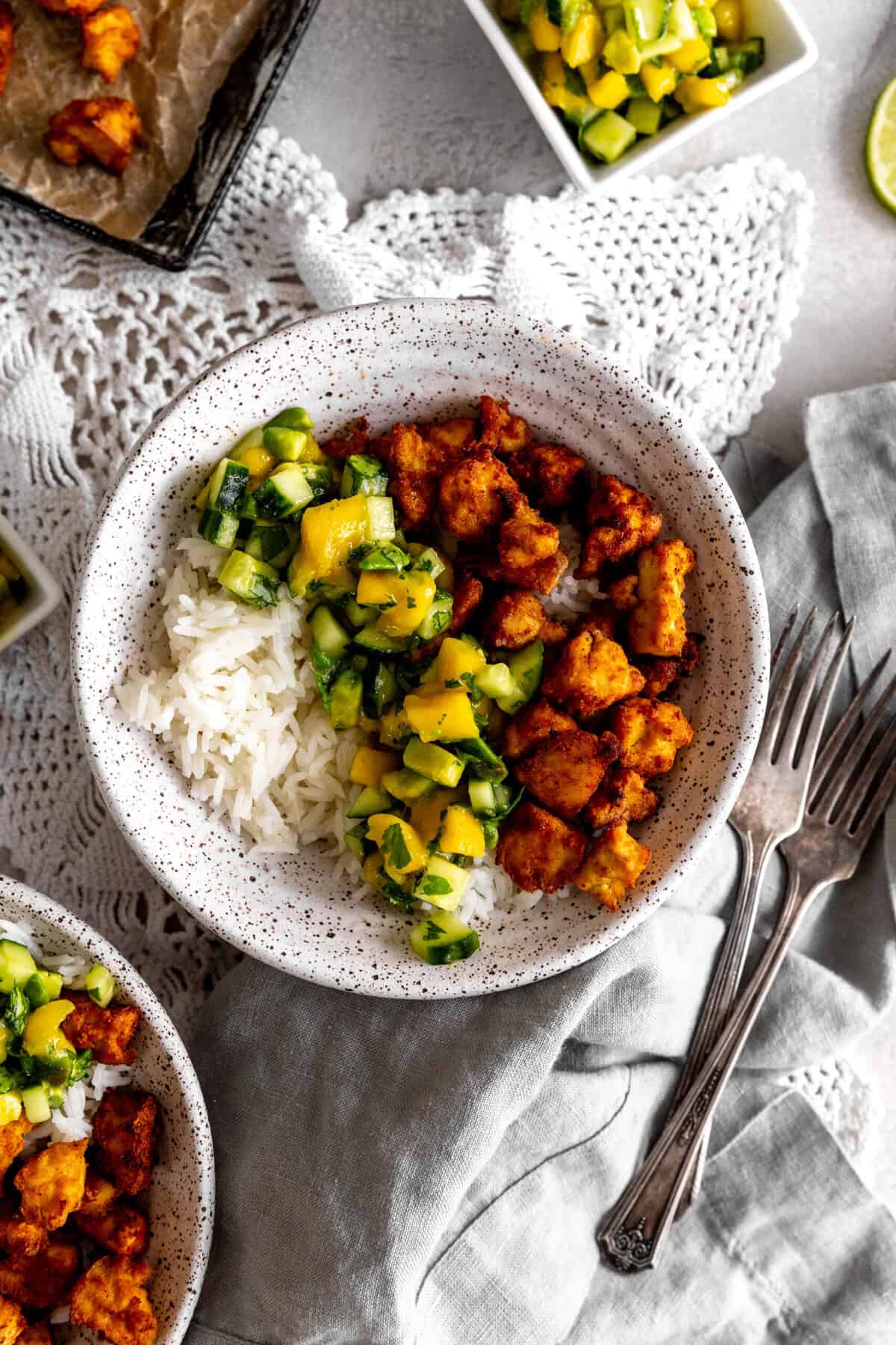 Bowl of mango and cucumber salsa and spiced tofu with forks.