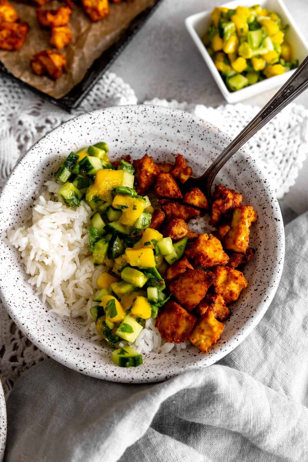 Fork in a bowl of spiced tofu, cucumber salsa and rice.