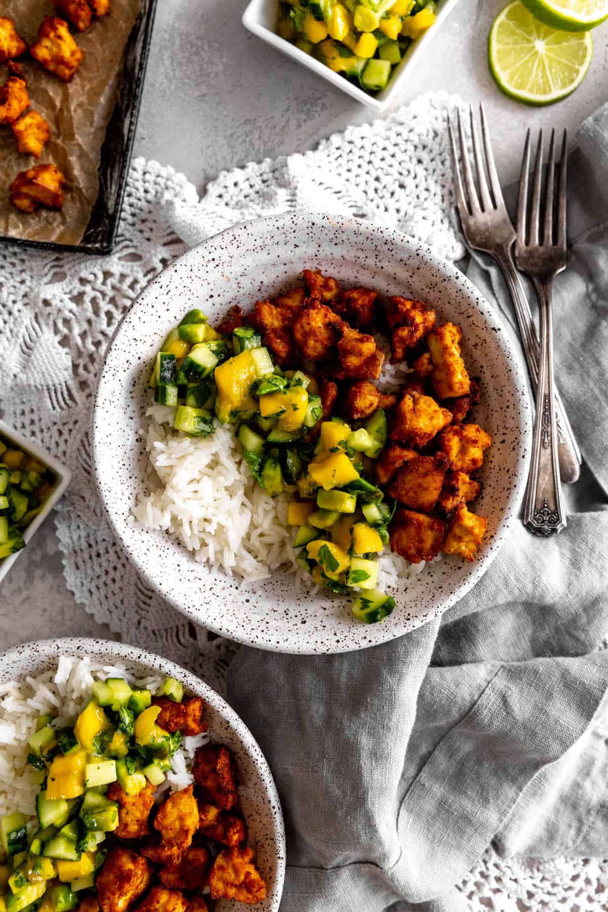 Bowls of spiced tofu, cucumber salsa and rice with forks and a baking sheet of tofu.