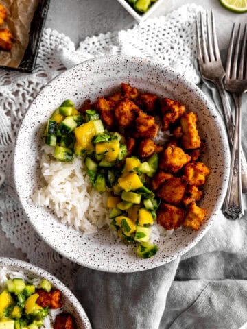 Bowl of spiced tofu, cucumber salsa and rice with forks and a napkin.