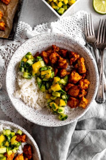 Bowl of spiced tofu, cucumber salsa and rice with forks and a napkin.