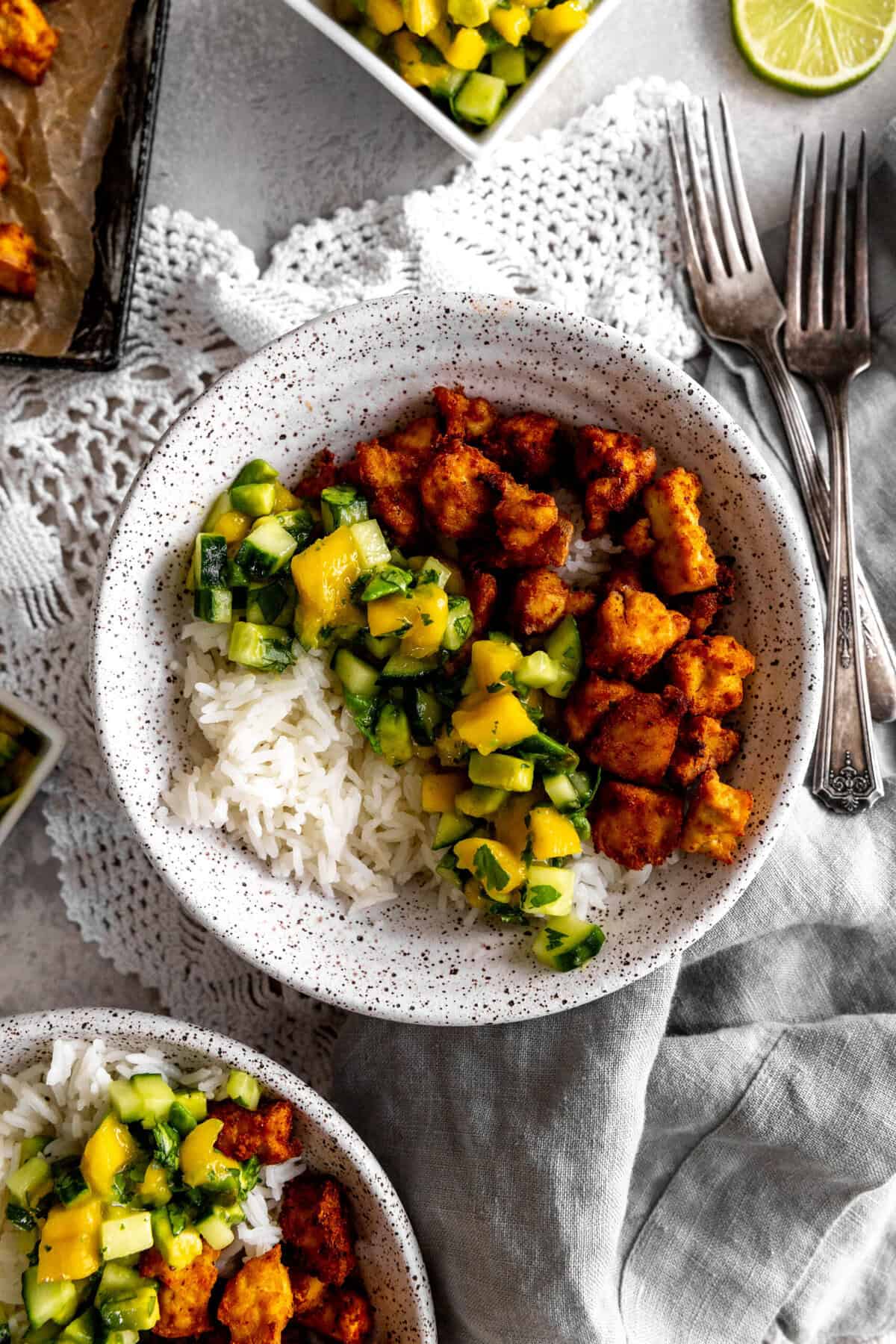 Bowls of spiced tofu, cucumber salsa and rice with forks.