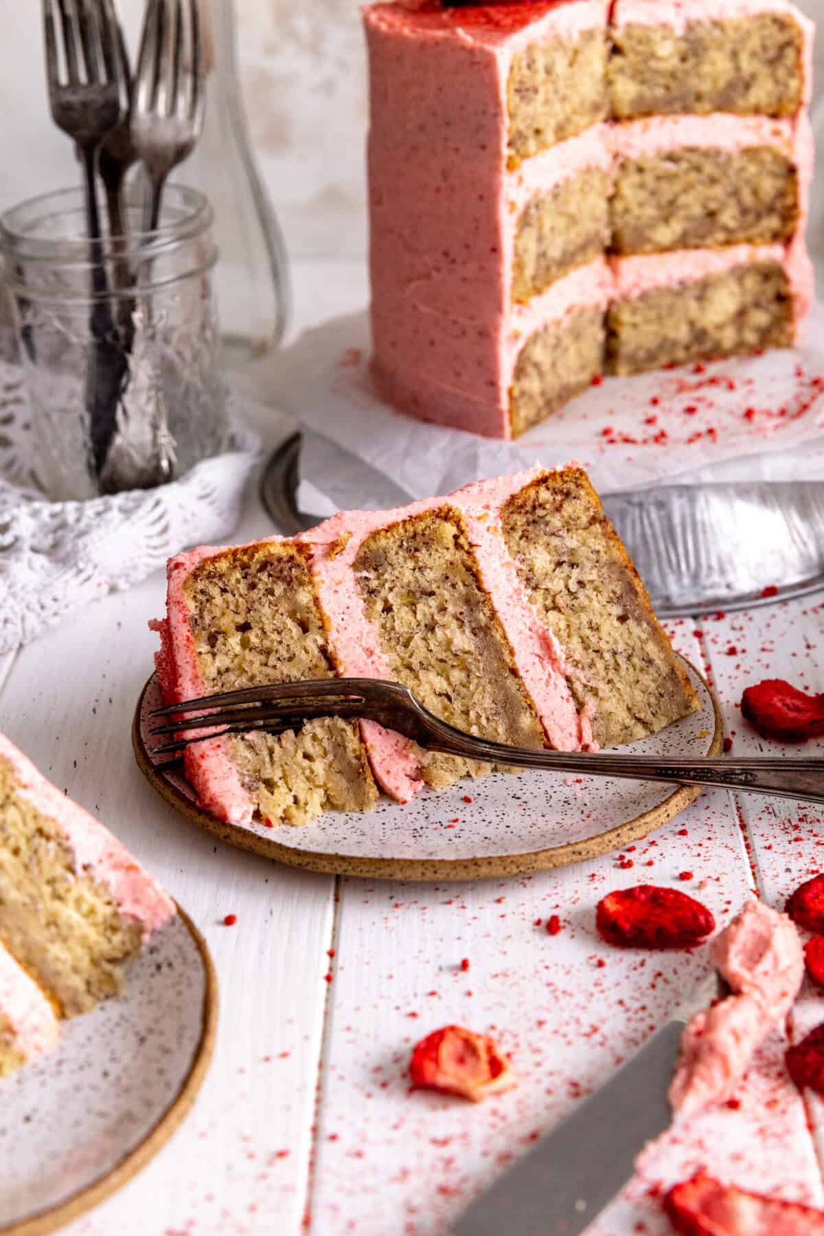 Fork cutting into a slice of cake with pink frosting on a plate