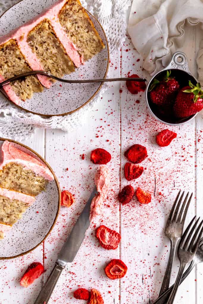 Slices of cake on plates and freeze-dried strawberries on a white background.