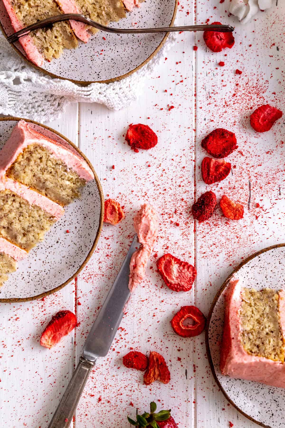 Slices of cake on plates and freeze-dried strawberries on a white background.