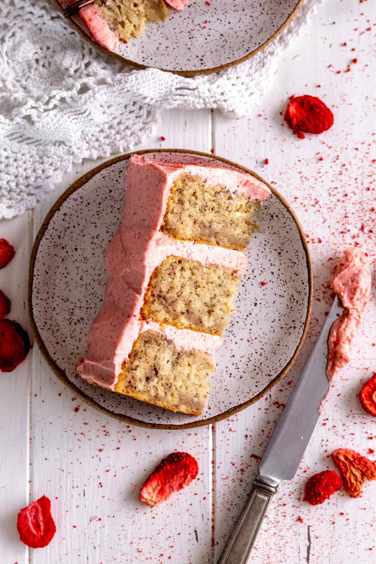 Slice of strawberry banana cake on a plate and a knife covered in frosting.