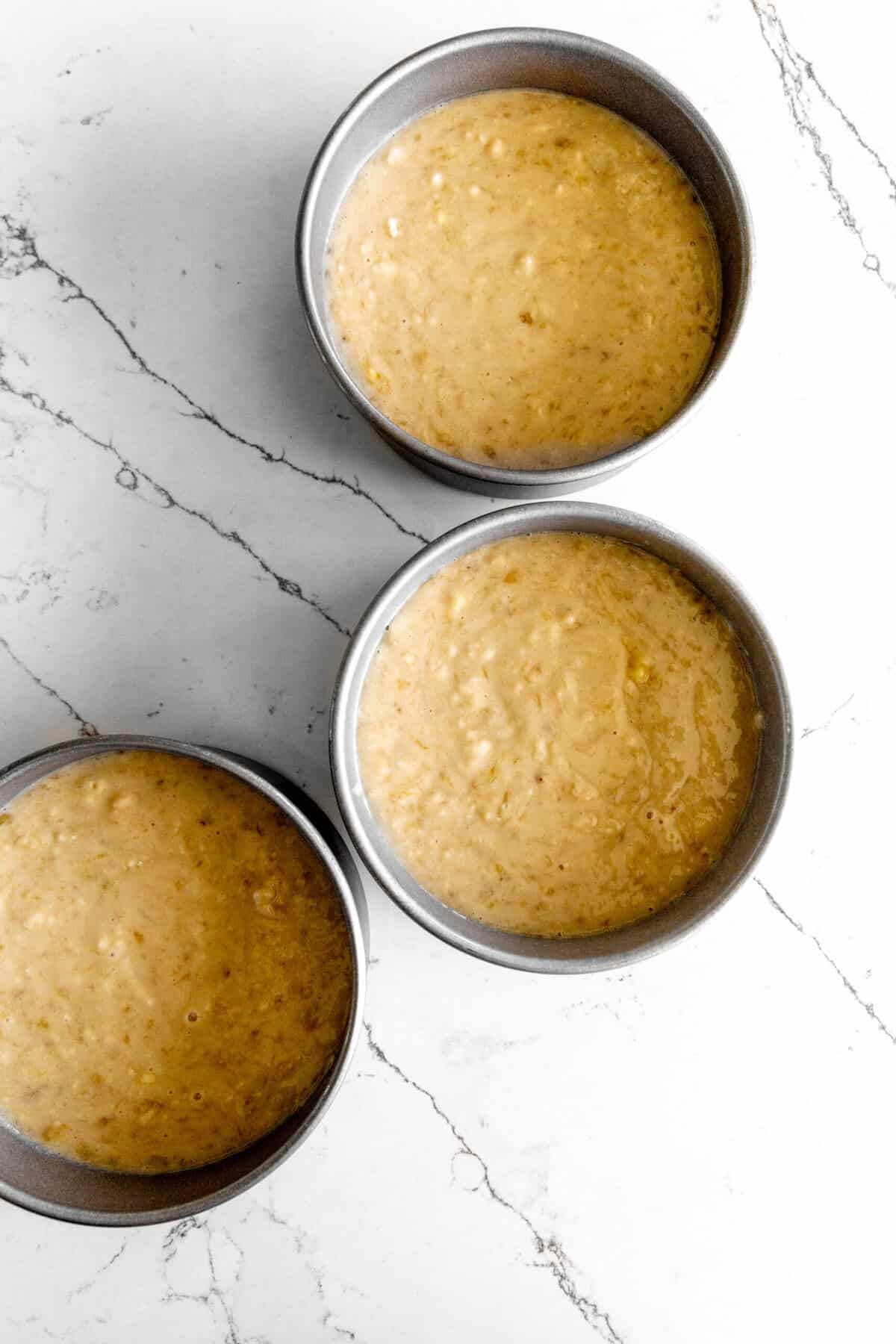 Three pans of unbaked cake batter sitting on a marble counter