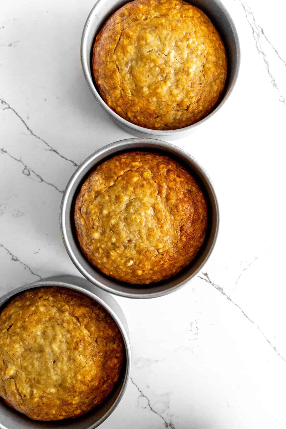 Three baked cake layers in pans on a white marble counter