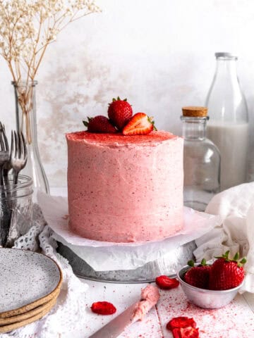 Pink cake with strawberries on top, a jug of milk and a cup of strawberries.