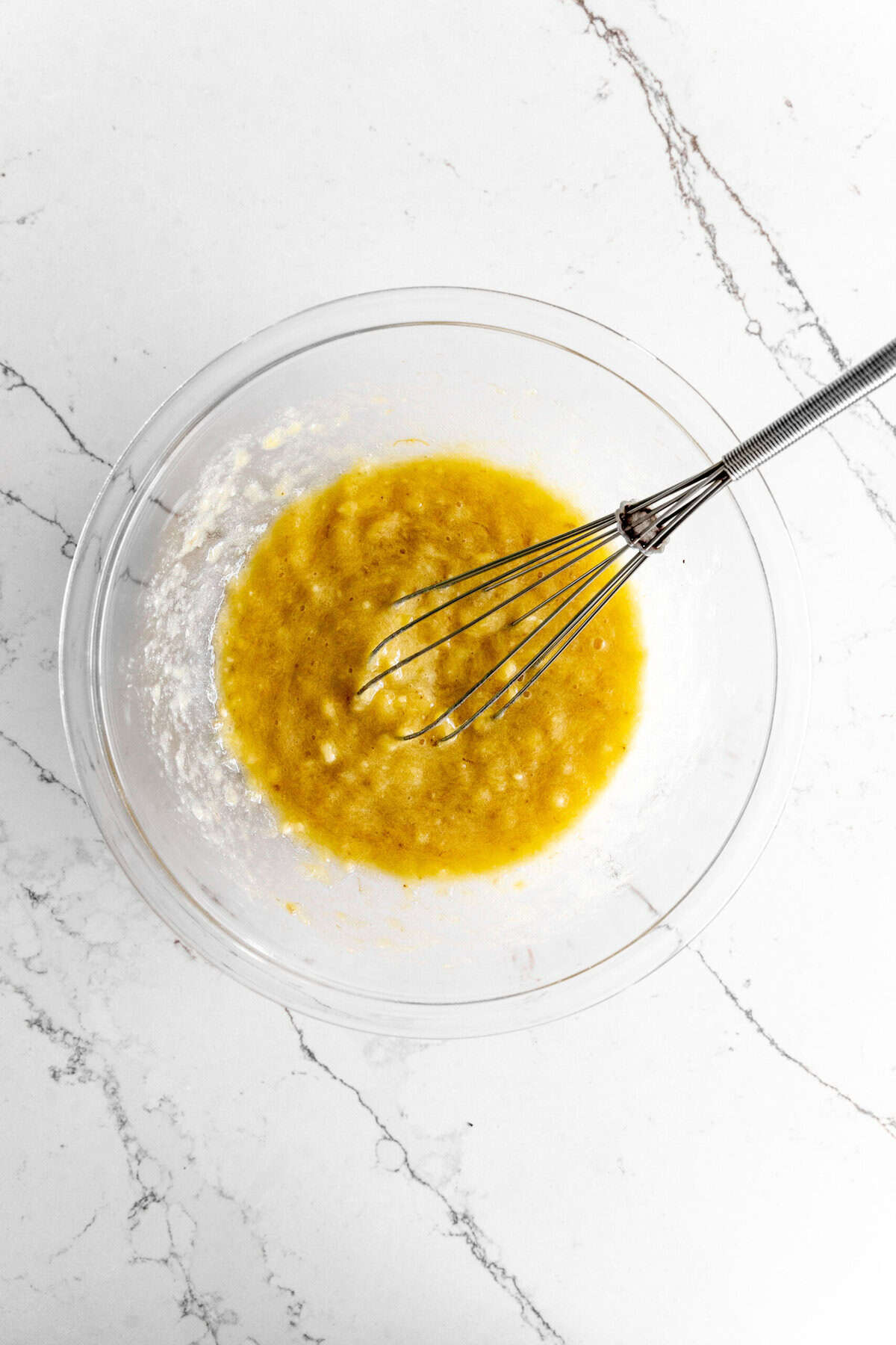 A bowl of mashed banana with a whisk.