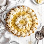 Banana cream pie, two cups of milk, banana slices and a stack of plates.