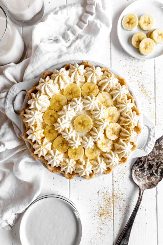 Banana cream pie, two cups of milk, banana slices and a stack of plates.