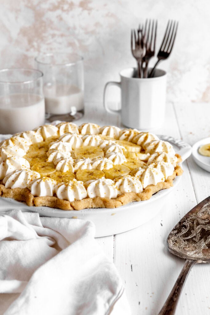 Banana cream pie, two glasses of milk, a cup of forks and a serving spatula.