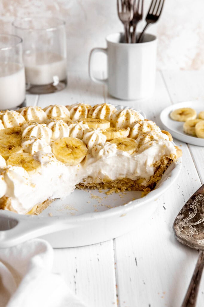 Banana cream pie with slices missing a a glass of milk.