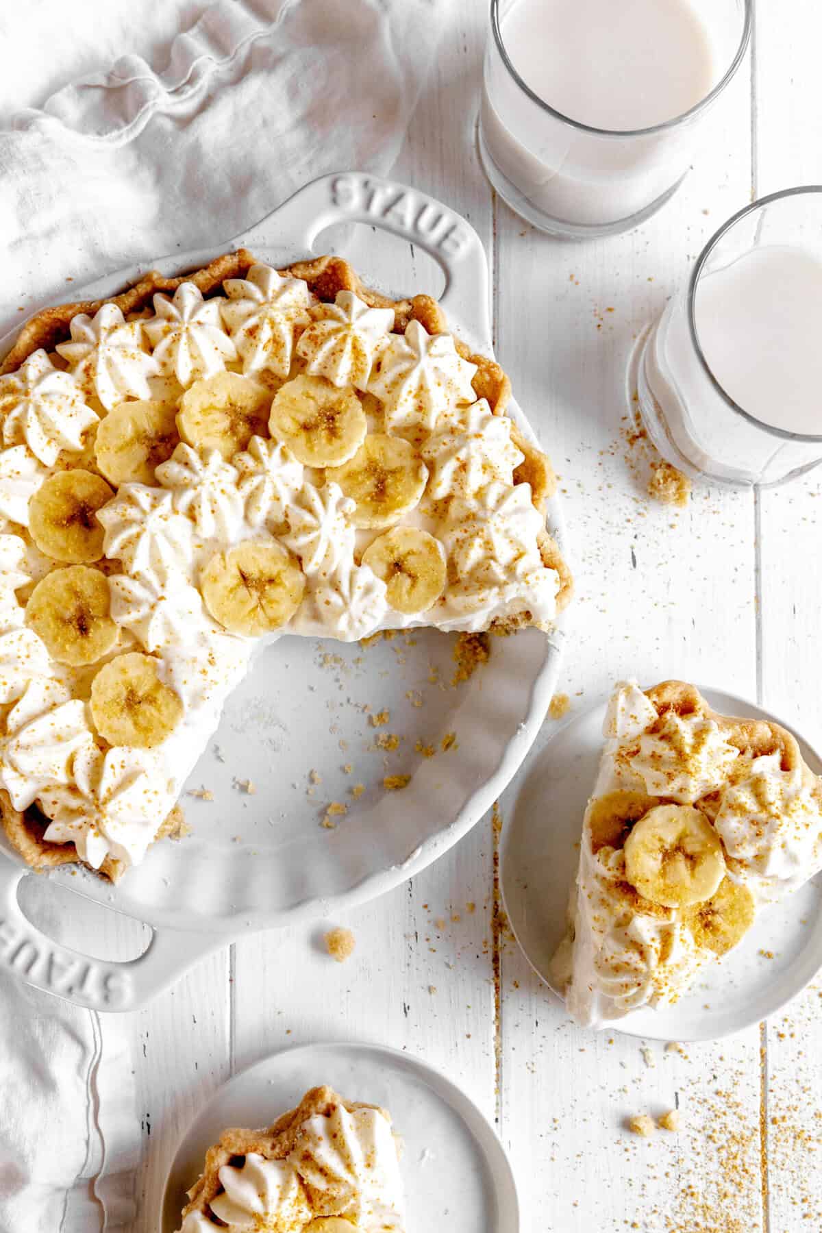 Banana cream pie, glasses of milk and slices of pie on white plates.