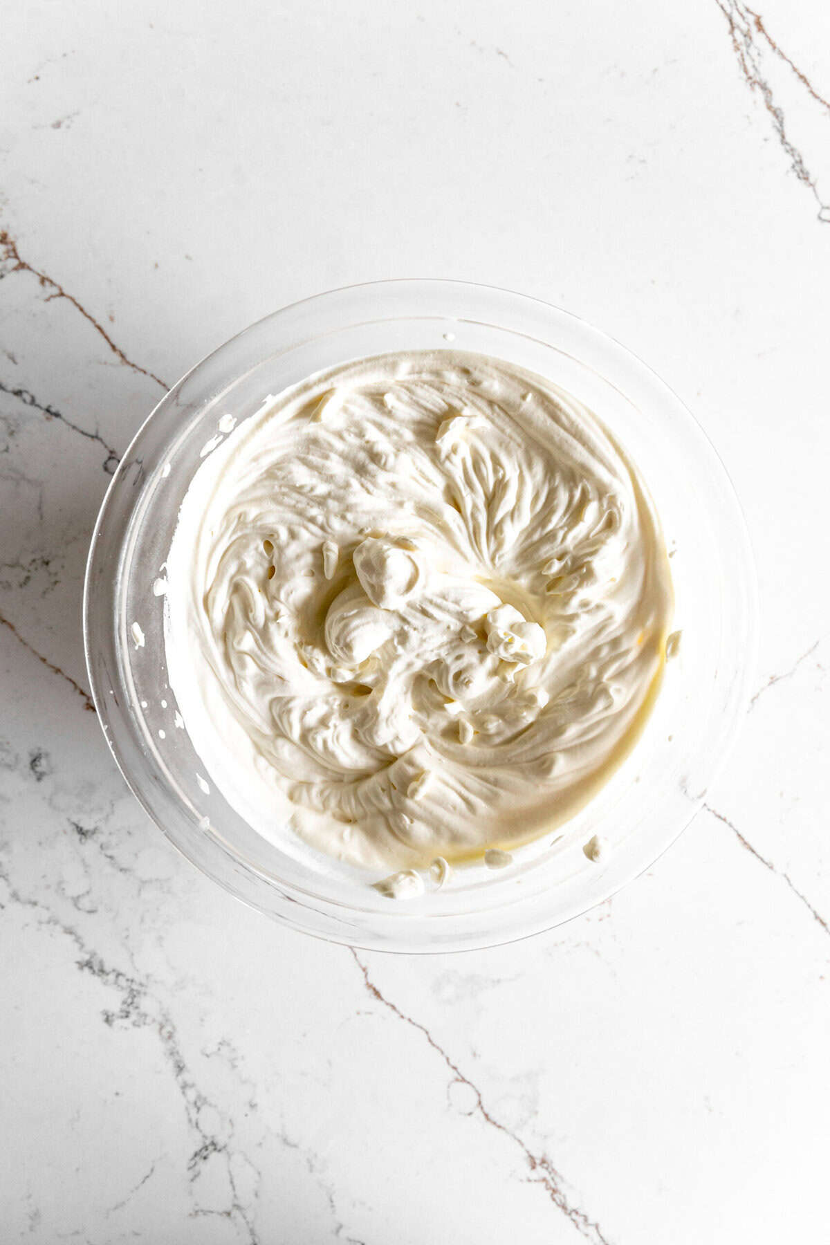 Glass bowl of whipped cream on a marble counter.