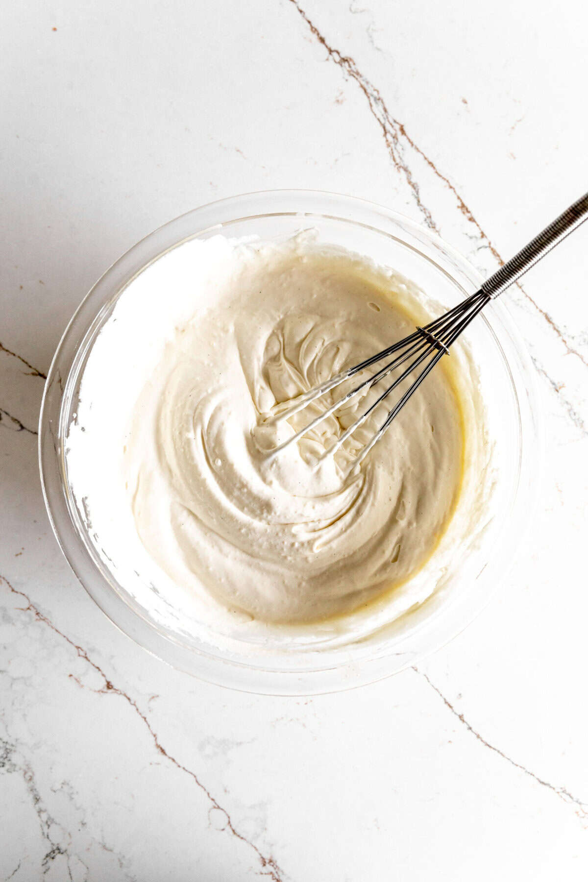 Banana cream pie filling in a glass bowl with a whisk.