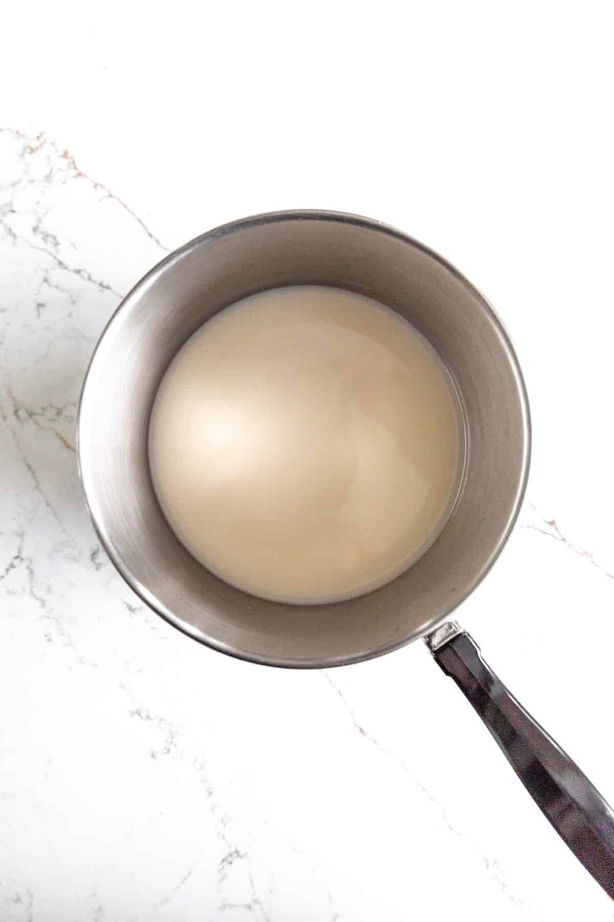 Saucepan filled with nondairy milk on a marble countertop.