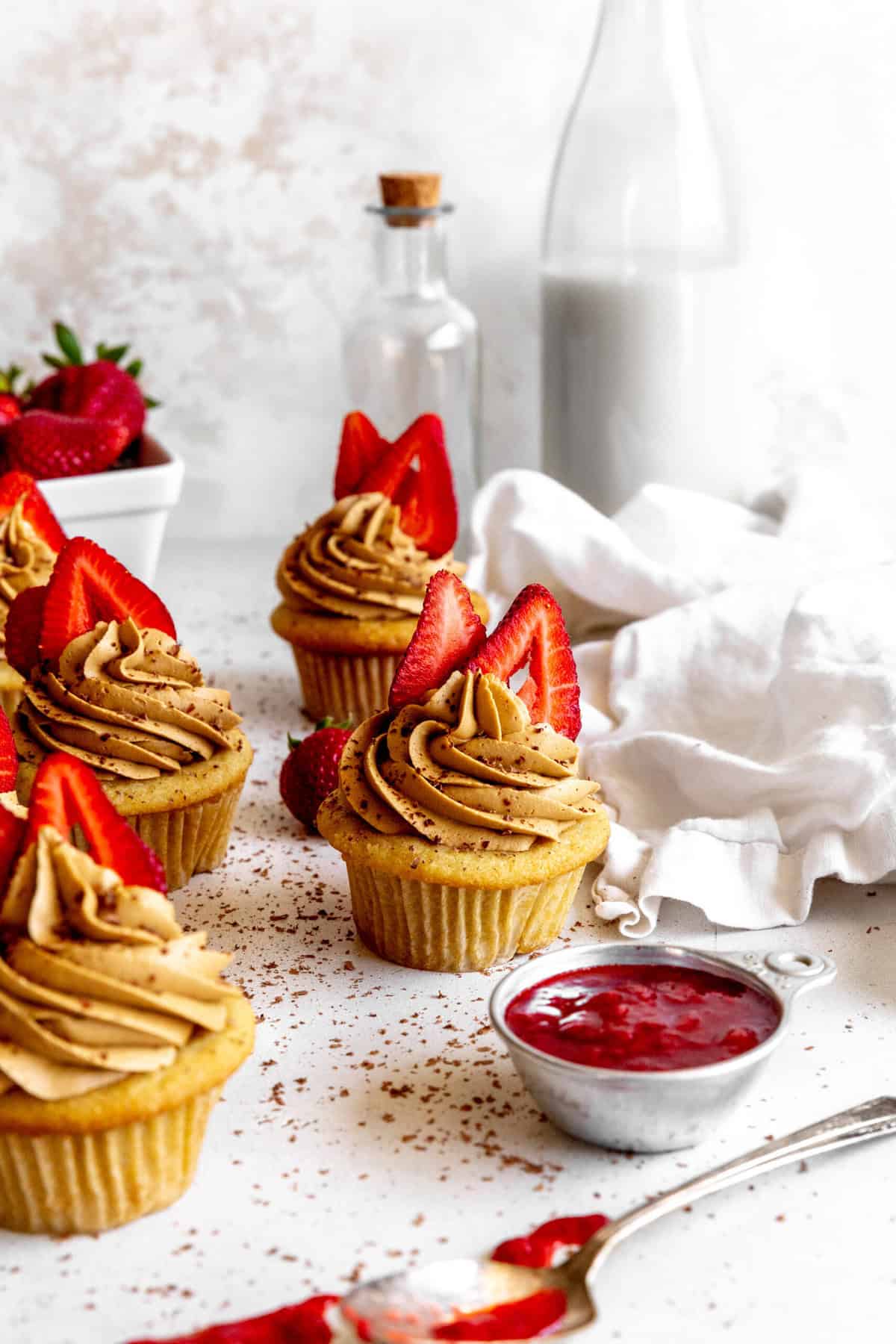 Cup of strawberry jam in front of strawberry tiramisu cupcakes.