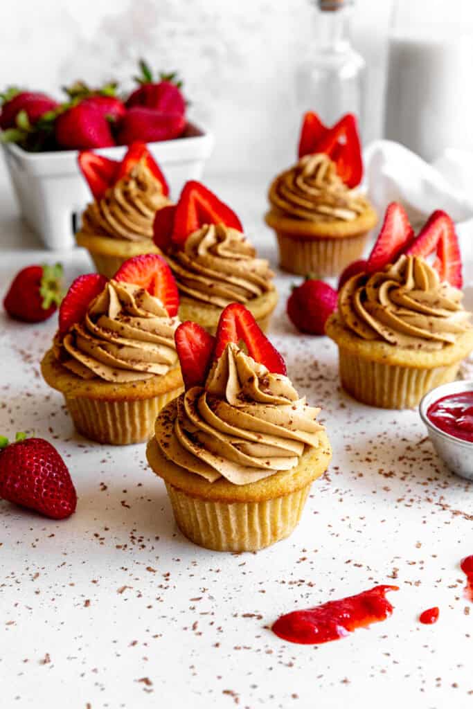 Strawberry tiramisu cupcakes, a basket of strawberries and a jug of milk.