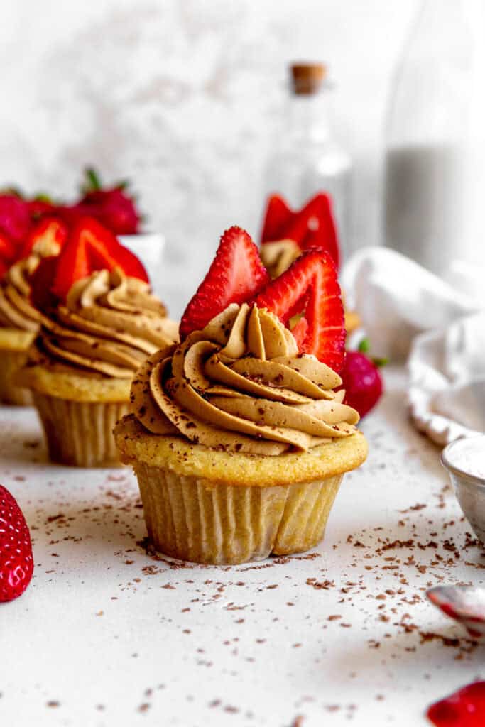 Cupcake topped with strawberries, a linen napkin and a jug of milk.