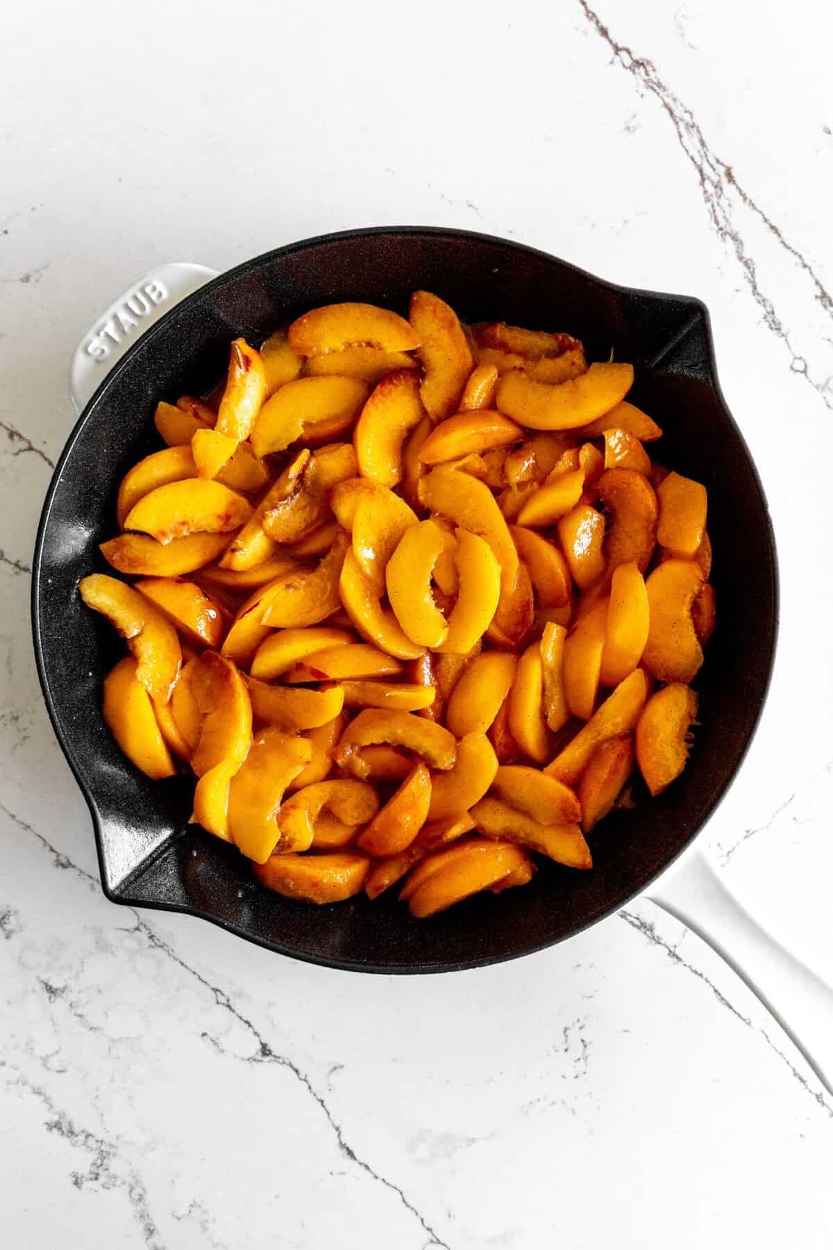 Peach slices spread out in a cast iron skillet.