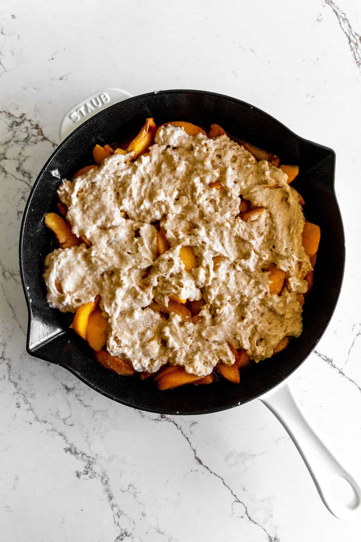 Unbaked peach cobbler in a cast iron skillet.