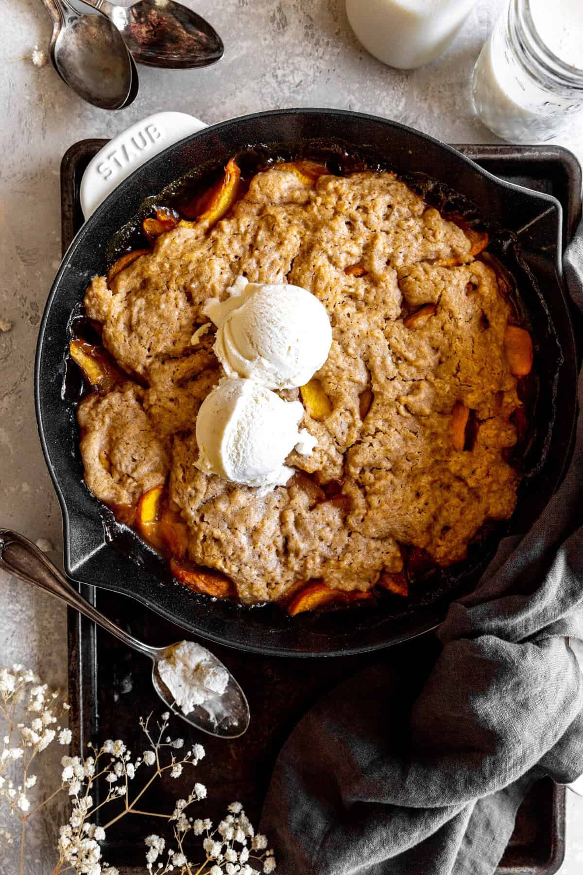 Peach cobbler topped with scoops of vanilla ice cream and a glass of milk.