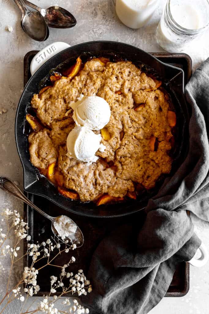 Peach cobbler topped with scoops of vanilla ice cream and a glass of milk.