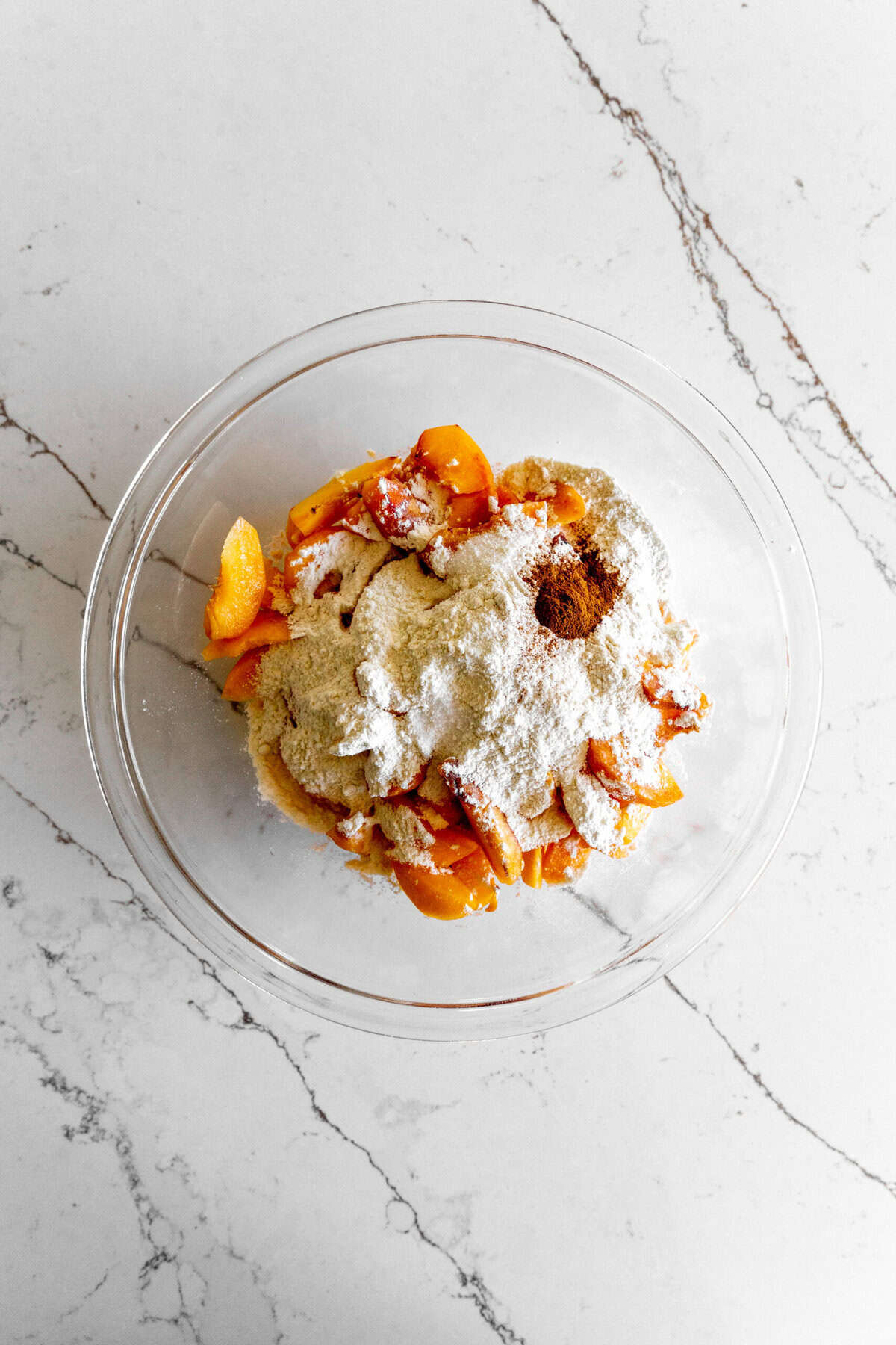 Peach slices covered in sugar, flour and spices in a glass bowl.