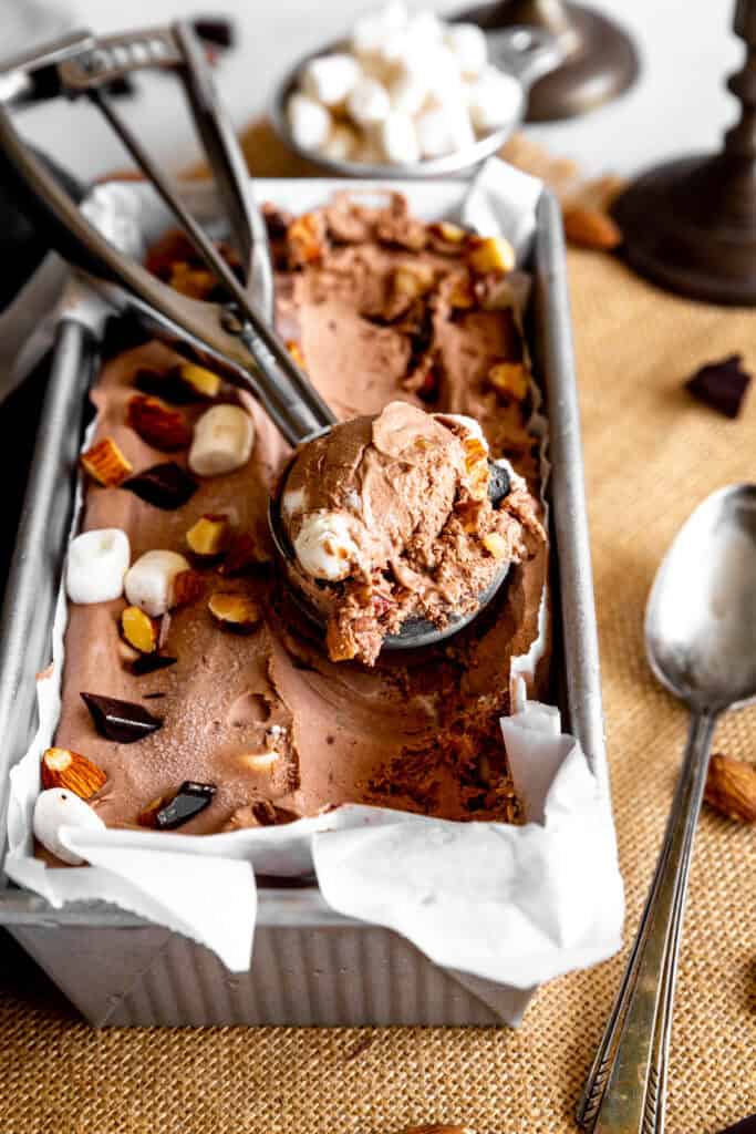 Ice cream scoop scooping rocky road ice cream in a loaf pan.