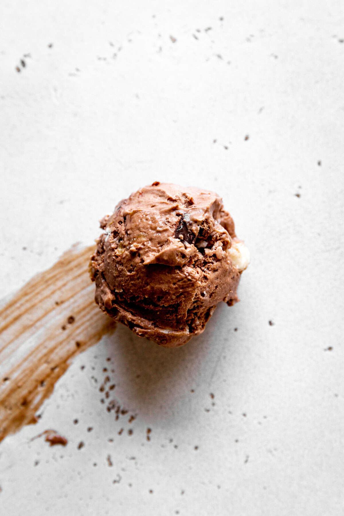 Scoop of rocky road ice cream sliding across a white surface.