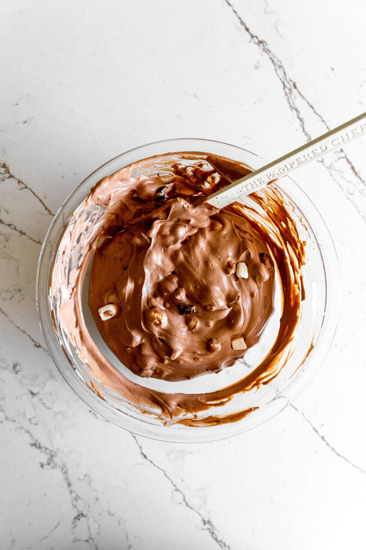 Unfrozen rocky road ice cream mix in a glass bowl with a rubber spatula.