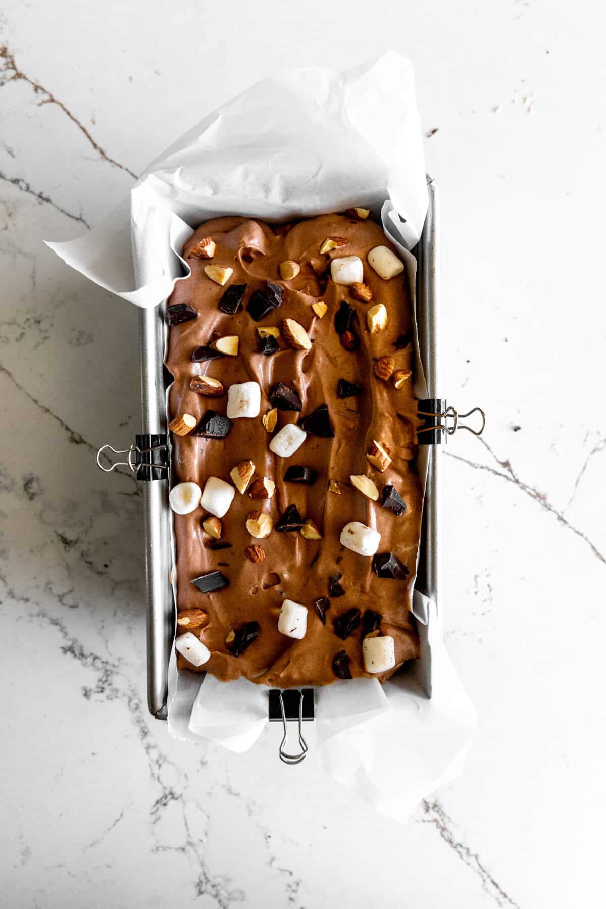 Unfrozen rocky road ice cream in a loaf pan lined with parchment paper.